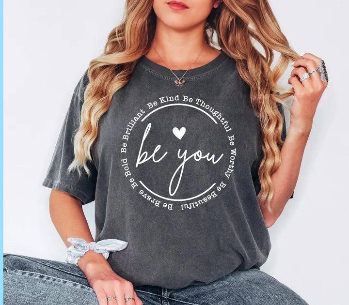 a woman sitting on a chair wearing a t - shirt that says be you