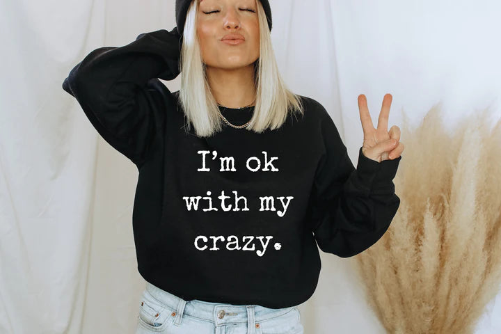 a woman wearing a black sweatshirt that says i'm ok with my crazy